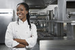 © moodboard - Portrait of a smiling female chef with hands crossed in the kitchen