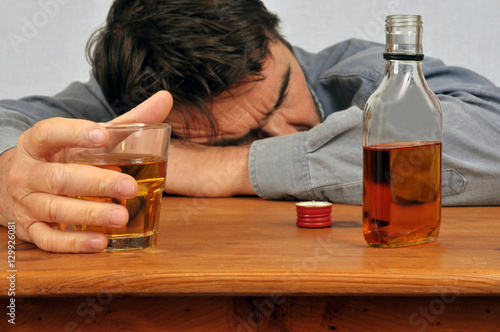 Fotografía Homme ivre endormi sur une table avec un verre de whisky en main