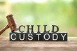 Text CHILD CUSTODY made of black blocks and letters with judge gavel on table against blurred background, closeup