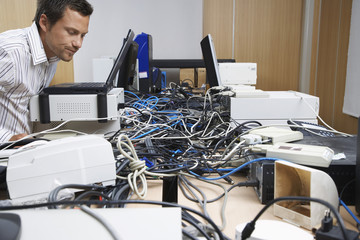 Side view of a male office worker looking at wire mess connecting computers and printers in office