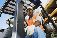 Low Angle View Of A Happy Male Industrial Worker Driving Forklift At Workplace