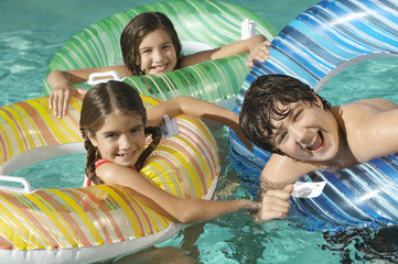 Wall Mural - Portrait of a three playful siblings with inflatable rafts enjoying together in swimming pool