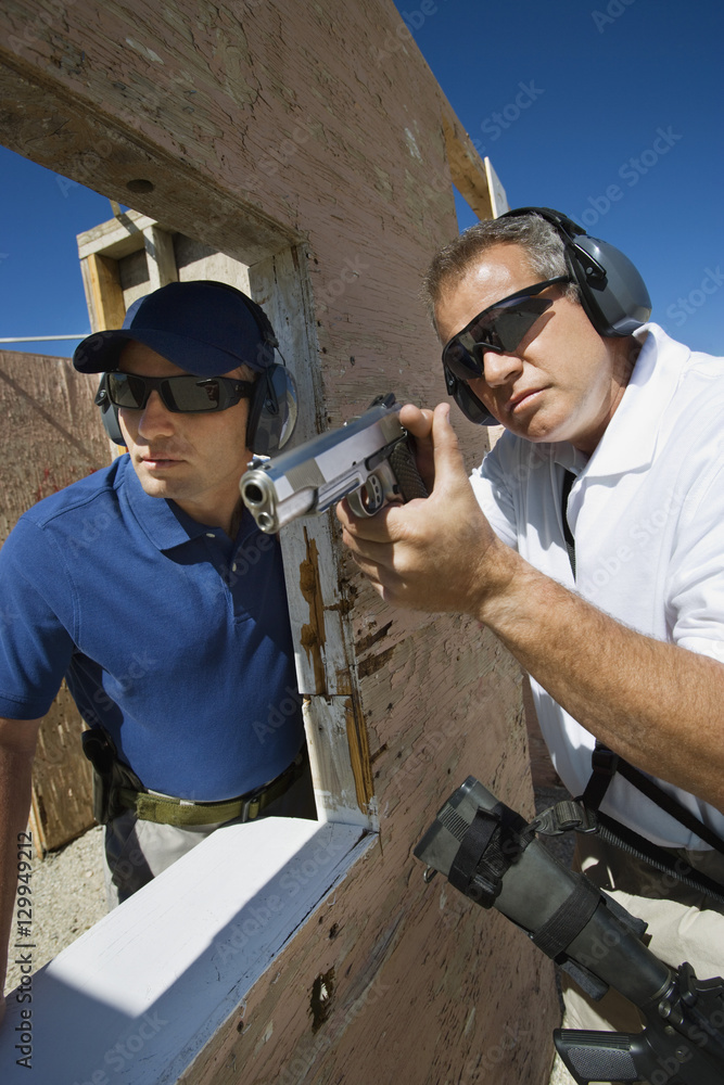 Gun Range Intructure Instructor assisting man with hand gun at firing range during combat ...