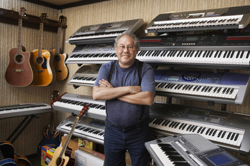 Portrait of middle aged male music store owner standing arms crossed