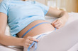 © MDBPIXS - Closeup midsection of a pregnant woman measuring stomach on bed