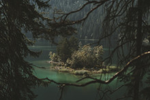 Island With Wild Trees In A Lake Surrounded By A Mountain Forest And Framed By Branches