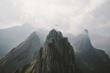 Paraglider Flying Over Tall Mountain Structure And Through Clouds On A Bright And Hazy Day