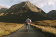 © Michael Schauer - Adventurous Young adult male wearing jeans and a colorful flanel shirt running down a road towards a mountain at sunset