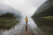 © Michael Schauer - Young adult male wearing yellow jacket standing on a footbridge at a foggy mountain lake with forest