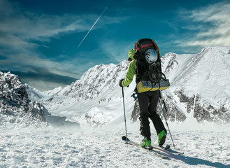 Men with backpack at ski goes to the top of mountain in sun day