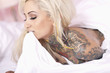 Sexy tattooed woman biting bed sheet