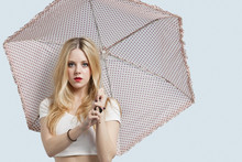 Portrait Of Young Woman Holding Polka Dotted Umbrella Against Light Blue Background