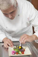 Wall Mural - Male chef arranging edible flowers on salad in commercial kitchen