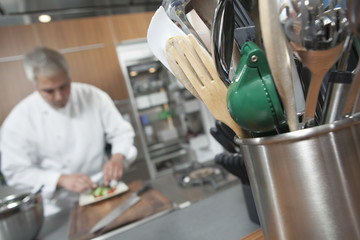 Wall Mural - Male chef working with focus on utensil holder in foreground