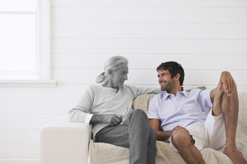 Senior man sitting on sofa at porch with mid adult son