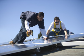 Two engineers working on solar panels against blue sky