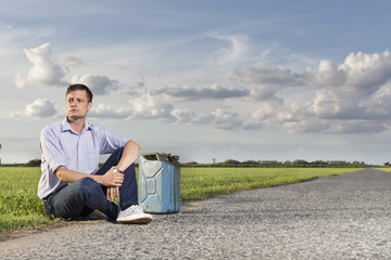 Wall Mural - Full length of young man with empty gas can sitting by country road