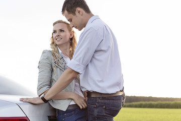 Wall Mural - Romantic young couple leaning on back of car at countryside