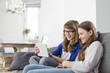 © MDBPIXS - Happy sisters using digital tablet on sofa at home