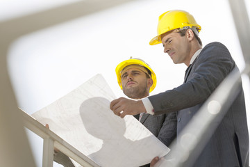 Low angle view of young businessmen holding blueprint against clear sky