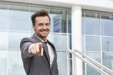 Portrait of happy businessman pointing at you outside office building