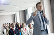 © MDBPIXS - Businessman pointing while speaking through microphone during seminar in convention center