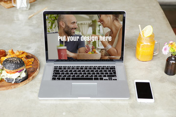 Technology, business and working process. Front view of workspace of freelancer: open laptop computer with copy space for your design, resting on table with smart phone, orange juice and burger