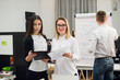 © romankosolapov - Two beautiful office workers having conversation while man colleague drawing business strategy on flip chart.