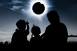 Silhouette back view of family looking at solar eclipse on dark sky