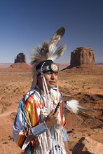 Navajo Man In Traditional Costume, With Merrick Butte On The Right And East Mitten Butte On The Left In The Background, Monument Valley Navajo Tribal Park, Arizona