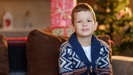 A boy dressed in a warm jacket sits on a coach in a room with Ch