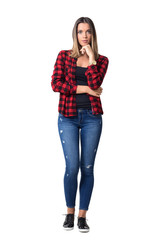 Wall Mural - Gorgeous pensive casual woman in red checkered shirt with hands on chin looking at camera. Full body length standing portrait isolated over white background.