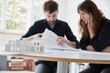 © Mint Images - A modern office. Two people at a meeting discussing plans and architectural drawings. A small-scale model building in the foreground