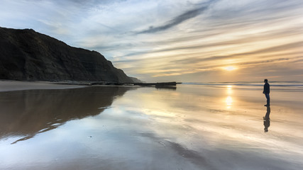 A Man contemplating the nature on a isolated beach. Sunset and the reflections on the sand