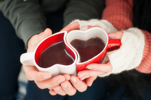 A Couple In Love Warming Hands With Hot Mug Of Tea. Mug In Shape Of Heart