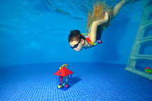 Sports Little Girl Dressed In Carnival Costume Dives To The Bottom Of The Pool For A Toy Gift. Portrait. Shooting Underwater. Landscape Orientation