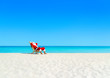 Christmas Santa Claus tan relaxing on sunlounger at sandy beach.