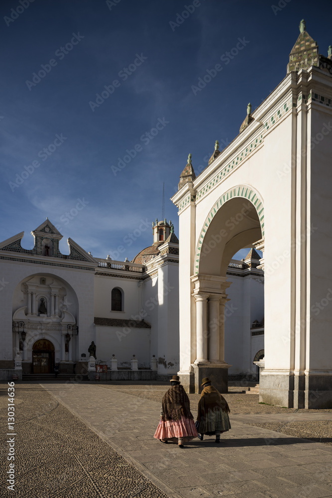 Traditionally dressed women walking past Copacabana Cathedral after dawn, Copacabana, Lake Titicaca, Bolivia