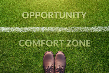 top view, male with leather shoes with a word : comfort zone and opportunity between a line on green