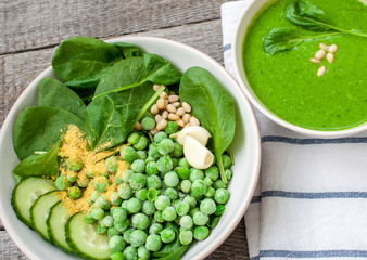 Wall Mural - Green peas spinach basil pesto and Ingredients in a white bowl on a wooden background. Love for a healthy raw food concept.