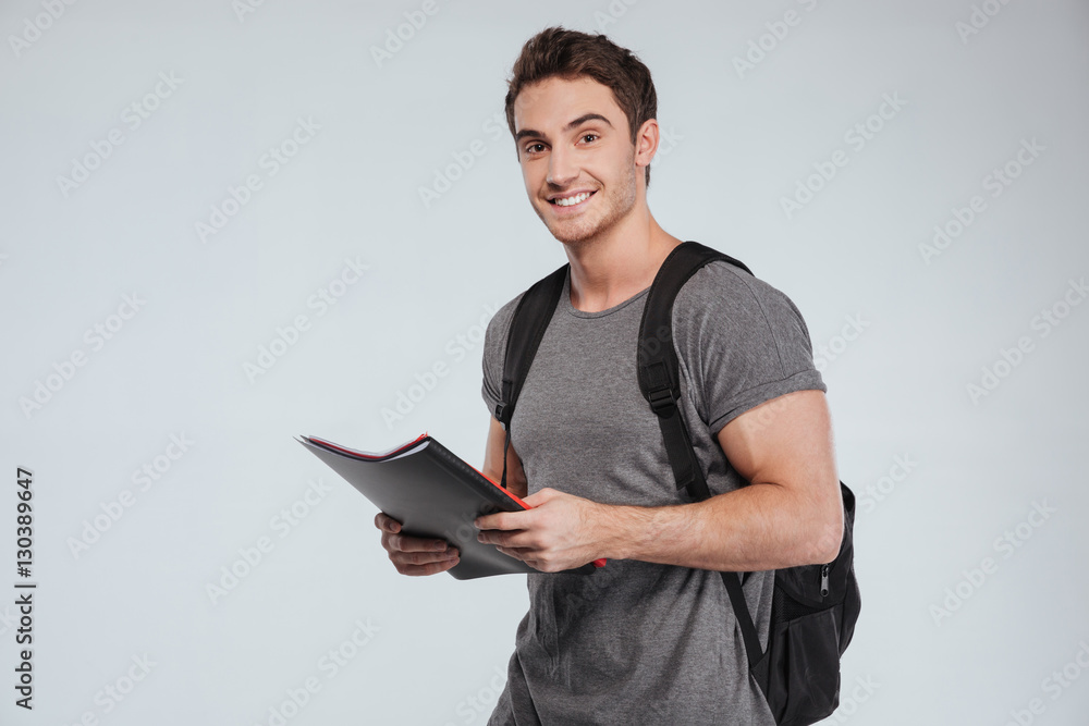 Smiling male student standing with folders and backpack Stock Photo ...
