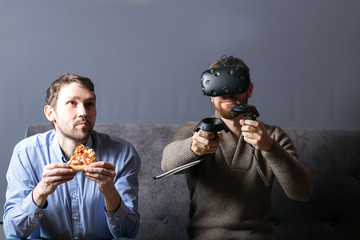 man using virtual reality headset and his friend eat pizza