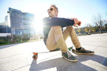 Wall Mural - Trendy urban guy sitting on skateboard in park