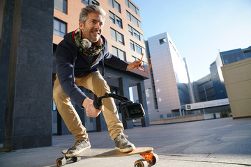 Wall Mural - Mature man skateboarding in urban environment, filming himself