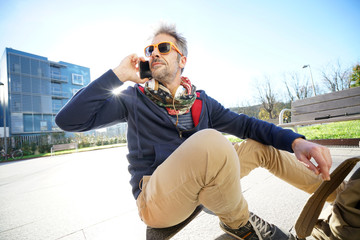 Man sitting on skateboard and using smartphone