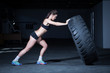 Female fitness model flipping a tyre in a gym