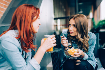 Two girls sitting in a bar having fruit salad and juice talking - best friends, chatting, gossip concept