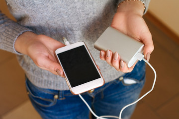 Two girls hands hold of the phone and charger. Powerbank and smartphone in girl's hands. Energy charger power bank smart phone. Still life modern digital concept.