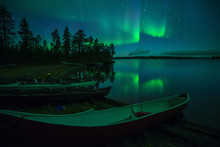 Beached Canoes And Aurora Borealis And Stars Reflected In Lake At Night, Muonio, Lapland, Finland