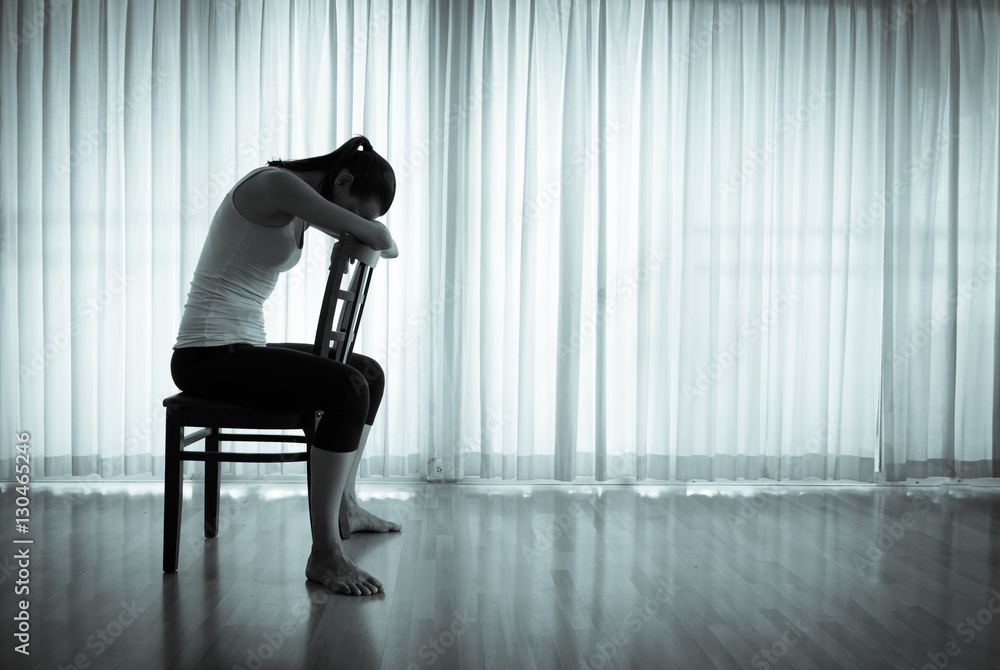 Sad woman sitting on a chair alone in a dark room. Sadness stress, and ...